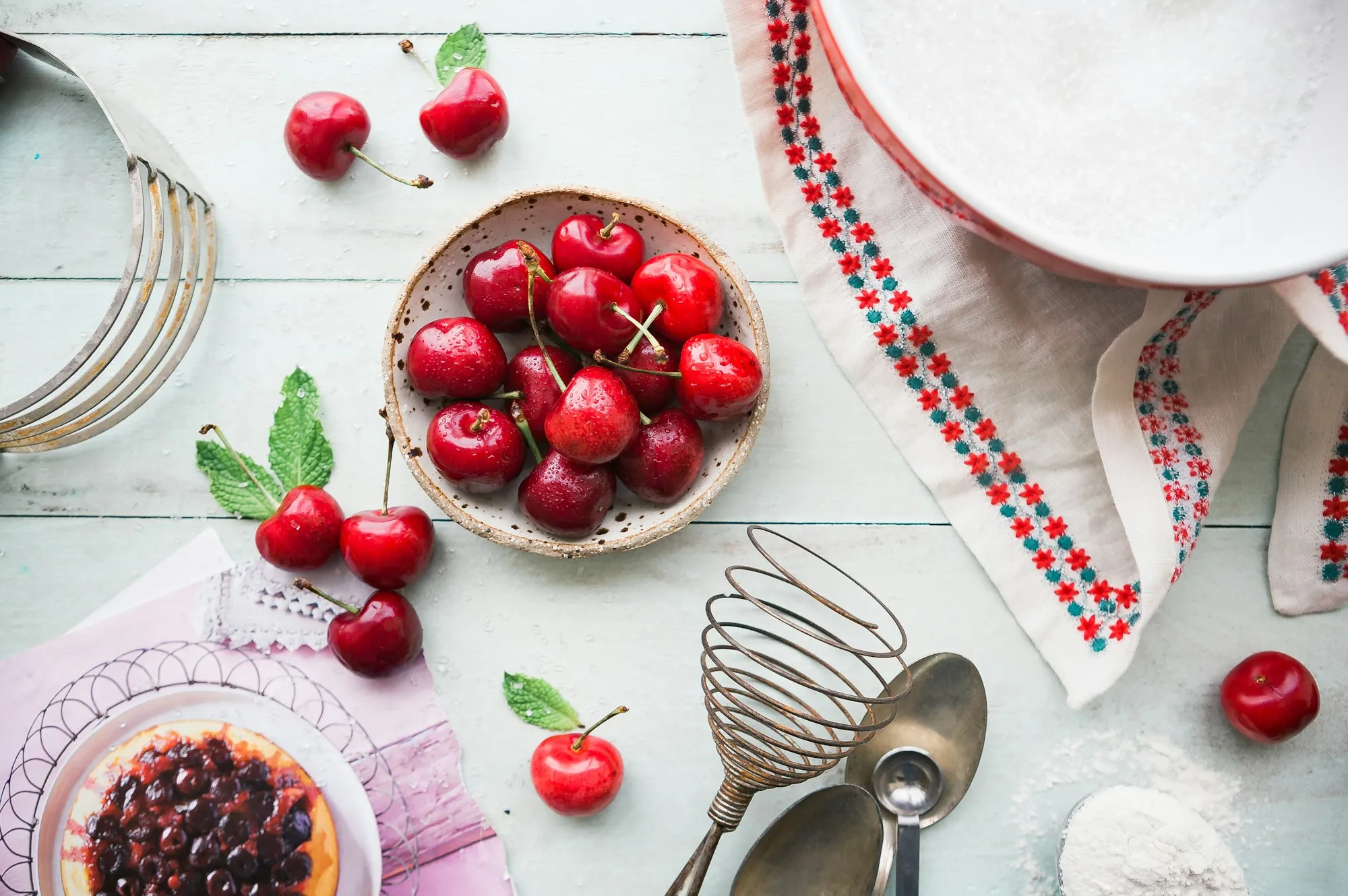 A ceramic bowl of ripe cherries on a pale wooden table