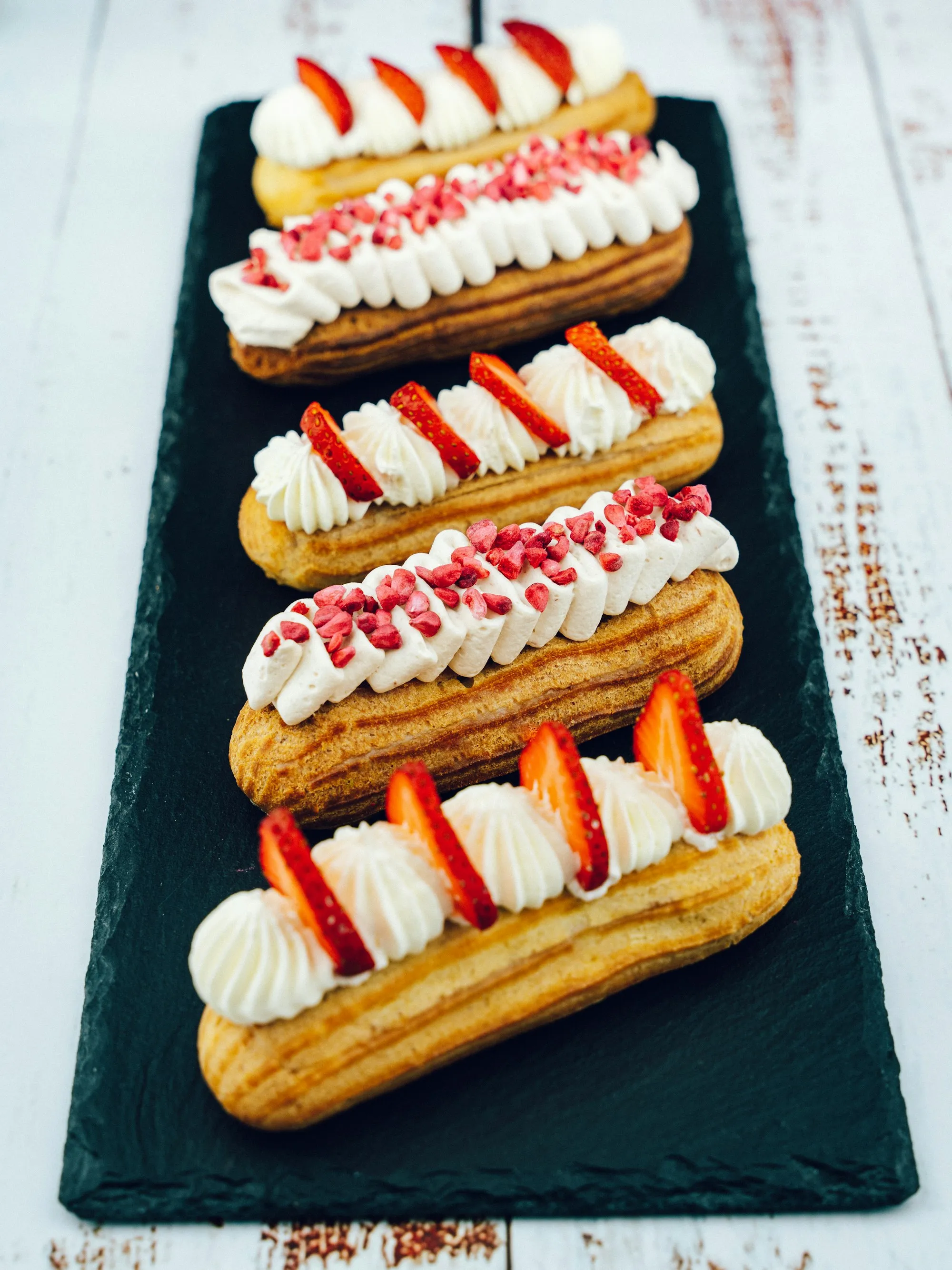 A row of strawberry éclairs on dark slate