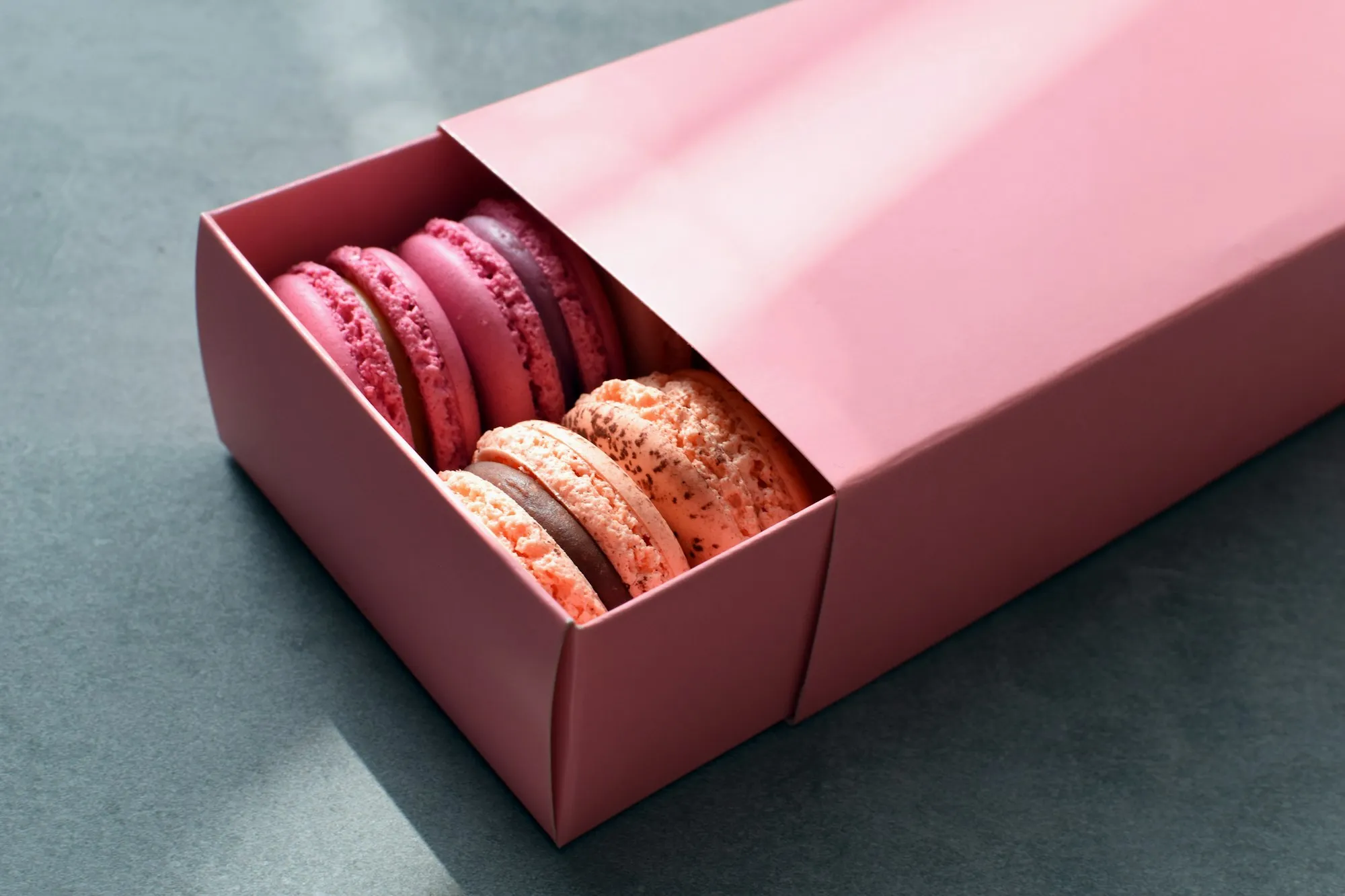 A pink gift box sliding open to reveal pink and coral macarons