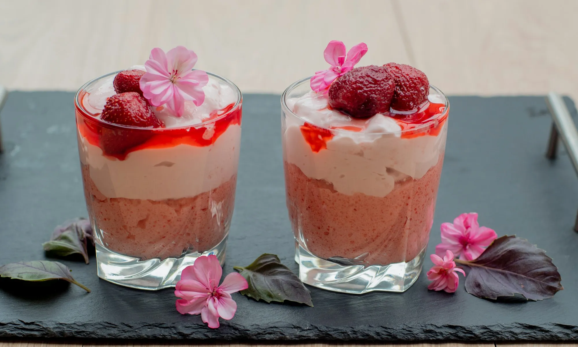 Two glasses layered with strawberry mousse and cream, topped with flowers